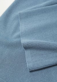 Jasnoniebieska dzianina o prążkowanej fakturze. Na zdjęciu widoczne są nakładające się fragmenty podkreślające miękki materiał i równy wzór ściegów.