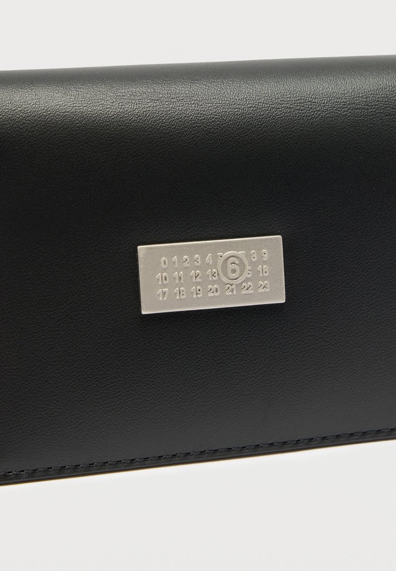 Sort læderpung med en rektangulær sølvplade med tal og et fremhævet "6", fremhævet af en enkel syningsdetalje.