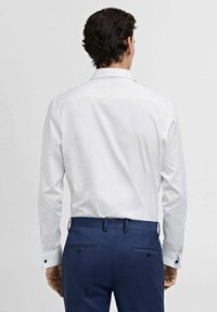 Weißes Hemd mit classic Kragen, langen Ärmeln und kontrastierenden schwarzen Manschettenknöpfen, kombiniert mit dunkelblauen maßgeschneiderten Hosen.