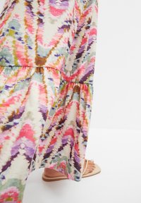Maxi sukienka ma żywy wzór tie-dye w odcieniach różu, fioletu, zieleni i brązu, z warstwowym krojem i miękkim, teksturowanym materiałem.