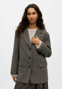 Dunkelgrauer Wollblazer mit Reverskragen, zwei Vorderaschen und drei Kn�öpfen. Darüber getragen ist ein hellbeiges Sweatshirt.