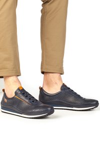 Sneakers in pelle perforata blu navy con suola in gomma bianca e nera, caratterizzate da dettagli arancioni e un design a profilo basso. Con lacci frontali.