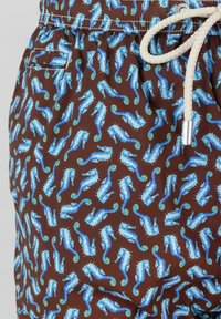 Bañador marrón con un patrón repetitivo de caballitos de mar azules, cintura elástica y cordón crema. El material parece ligero y suave.