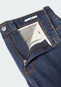 Jeans de denim azul oscuro con costuras naranjas, que cuentan con una cremallera frontal y cierre de botón. El interior tiene un forro de tela a rayas.