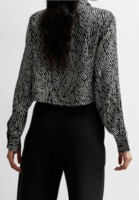 Blusa a maniche lunghe con motivo in bianco e nero, con una texture ondulata e una vestibilità ampia, abbinata a pantaloni neri.