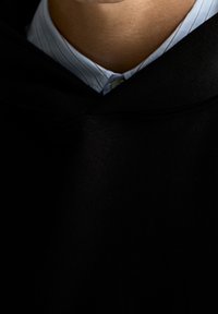 Czarna bluza z kapturem o teksturowanym wykończeniu, nałożona na jasnoniebieską koszulę z kołnierzykiem w cienkie paski. Charakteryzuje się luźnym dekoltem.