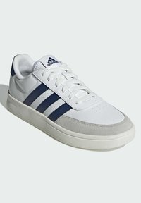 Bijela atletska cipela s mornarsko plavim prugama, gornjište od kože i semiša, vezanje na vezicu, podstavljeni ovratnik i teksturirana gumena potplat.