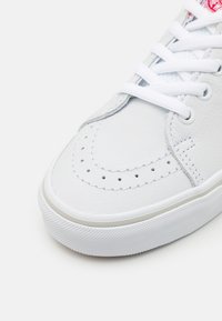 Baskets en cuir blanc avec embout perforé, lacets plats blancs et semelle en caoutchouc blanche texturée. Présente des détails de couture subtils.