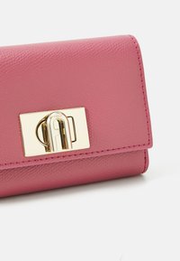 Pink textured leather wallet with a gold-tone metal clasp featuring a logo. The edges are stitched, highlighting the design details.
