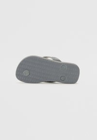 Semelle de tongs grise avec une surface en caoutchouc texturé, présentant deux points de cushioning circulaires et une légère courbure au niveau du talon.
