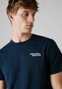 Marineblå bomulls-T-skjorte med en hvit "RED BULL RACING"-logo på venstre brystområde. Klassisk rund hals og korte ermer.