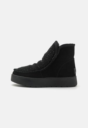 Botas altas negras de ante con detalle de cuentas texturizadas en la parte superior, que cuentan con una gruesa suela de goma negra y un cuello acolchado.
