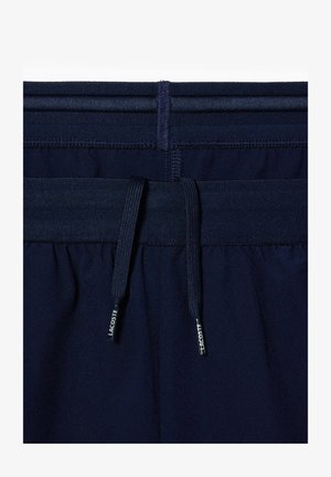 Calças de desporto azul marinho com um cós elástico e cordão. O material parece suave, com costuras limpas e detalhes de marca subtis.