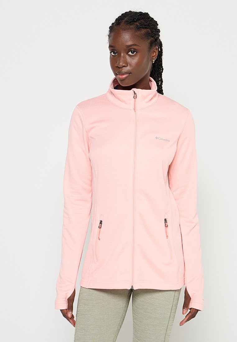 Chaqueta de forro polar de color rosa claro con un cuello alto, dos bolsillos con cremallera y un logotipo en la parte superior izquierda. Textura suave y diseño ajustado.