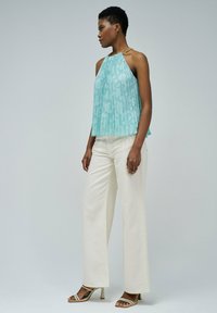 Un haut sans manches plissé, de couleur bleu clair, avec un motif texturé et un col halter, associé à un pantalon large blanc et des talons à lanières.