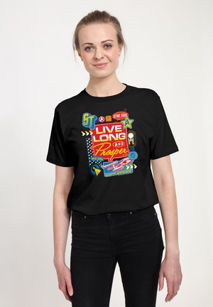 Vrouw met lichte huid en haar teruggebonden, die een zwarte Star Trek T-shirt draagt met de tekst "Live Long and Prosper" en bijbehorende afbeeldingen.