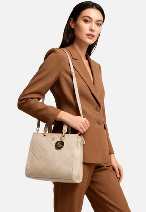 Borsa beige con design trapuntato, ferrature dorate e tracolla removibile. Indossata con un completo su misura marrone.