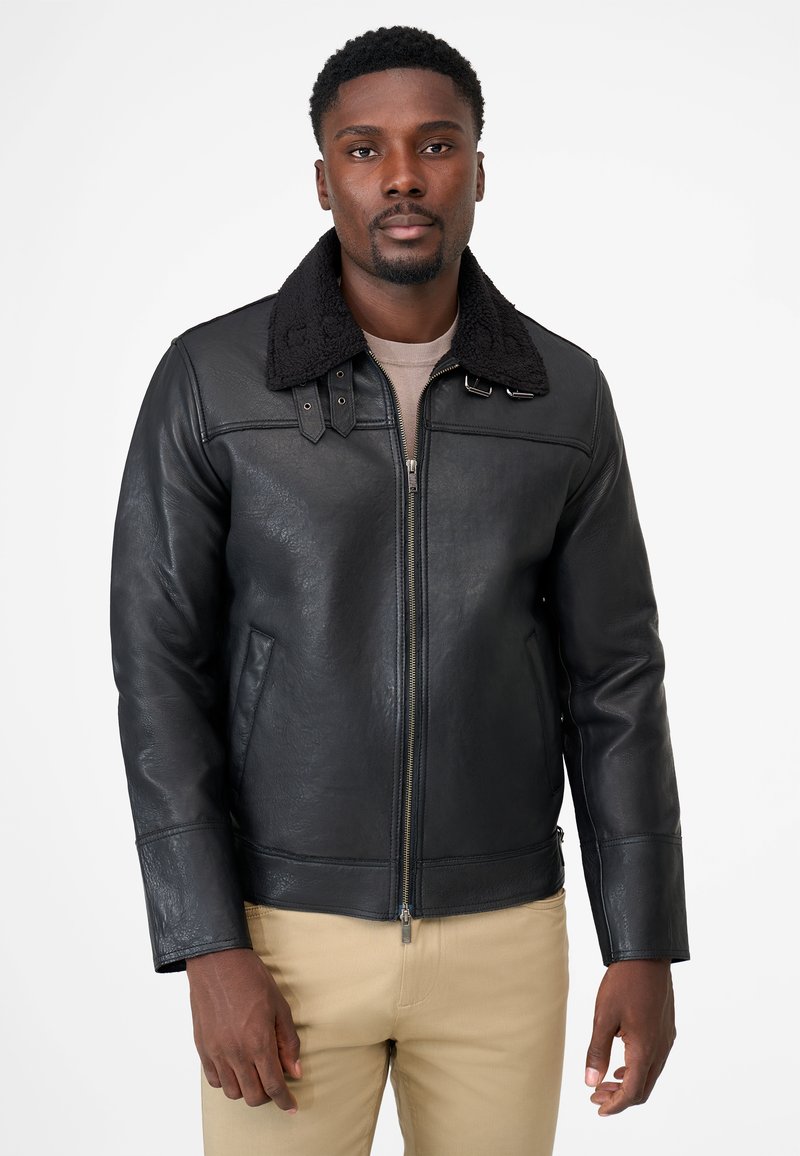 Black leather jacket with a shearling collar, zip front, and two front pockets. Smooth texture with pronounced seams and adjustable straps.
