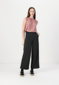 Haut sans manches rose avec un col froncé et des accents en dentelle, associé à un pantalon large noir taille haute et des baskets noires.