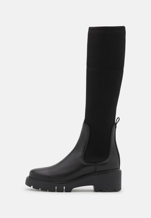 Bottines noires jusqu'au genou en cuir lisse avec un haut en tissu côtelé, un talon évasé et une semelle texturée pour une meilleure adhérence.