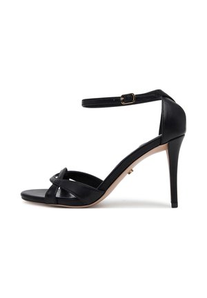 Black leather high-heeled sandals with an open toe, ankle strap, and crisscrossing front bands. Features a thin stiletto heel and tan sole.
