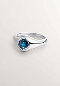 Anillo de plata con una banda curva y lisa. Presenta una piedra preciosa azul facetada engastada en un bisel redondeado, resaltando su color vibrante y brillo.