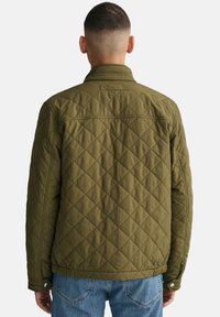 Jachetă quilted de culoare verde măslin, cu guler rotund, închidere cu capse și tiv elastic. Model cu romburi vizibile și țesătură texturată.