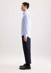 Lichtblauwe, lang mouw blouse met een klein stippenpatroon, gecombineerd met zwarte, op maat gemaakte broek en gepolijste zwarte schoenen.