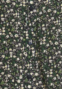 Camicia nera a bottoni con un motivo floreale in fiori bianchi e gialli, accentuata da foglie verdi. Tessuto testurizzato con bottoni visibili.