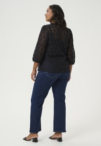 Blouse en dentelle noire avec des manches bouffantes, associée à un jean en denim bleu à jambes droites. Le haut présente un délicat motif floral.