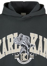 Mørkegrå hættetrøje med en hvid ørnerelief og store bogstaver "KARL KANI" på brystet. Stof ser blødt ud med en afslappet pasform ved hætten.