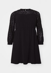 Robe noire avec un overlay en dentelle sur les manches longues, un col rond et une taille élastique, offrant une silhouette ample et fluide.