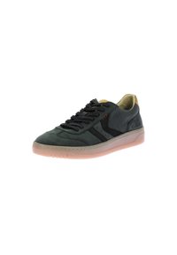 Baskets en suede vert foncé avec des accents noirs, une semelle intérieure jaune et une semelle en caoutchouc rose translucide. Comprend des lacets noirs et des coutures rouges.