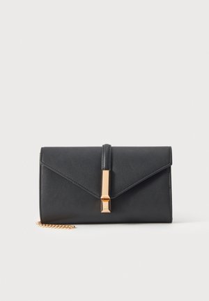 Pochette noire rectangulaire à rabat pointu, avec fermoir doré et courte bandoulière chaîne, présentée sur un fond uni clair.