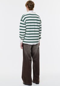 Koszula z długim rękawem w zielone i białe poziome paski, zestawiona z szerokimi spodniami z kordurowej tkaniny w kolorze brązowym. Prosty fason, luźny krój.
