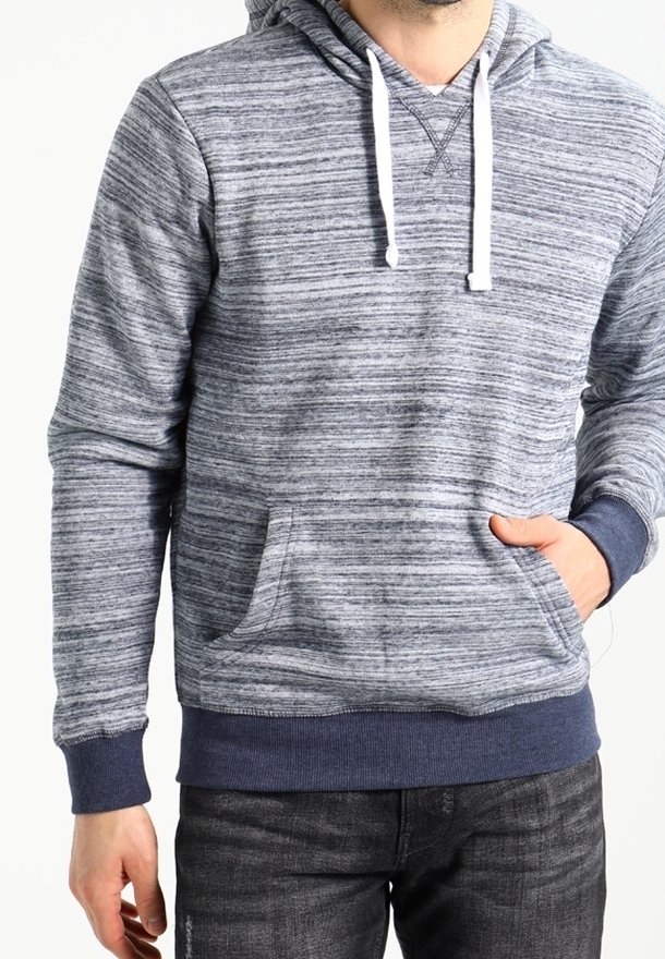 Homme portant un sweat à capuche gris et bleu marine rayé avec des cordons blancs, une main dans la poche avant, associé à un jean foncé.