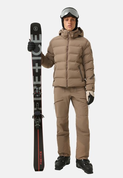 Braune Steppjacke, beige Hose, schwarze Handschuhe und Skistiefel. Hält schwarze Skier mit roten Akzenten und Bindungen. Glatte Texturen, modernes Design.