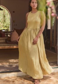 Robe maxi jaune avec un corsage ajusté et une jupe plissée fluide. Le tissu semble doux avec une légère texture. Présente un col rond.