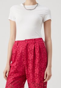 Vit åtsittande t-shirt med korta ärmar, parat med ljusrosa spetsbyxor med blommönster och knappstängning i midjan.