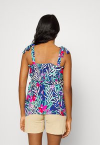 Top sans manches à imprimé floral avec des bretelles froncées, présentant des tons vifs de rose et de vert sur un fond marine, associé à un short beige.