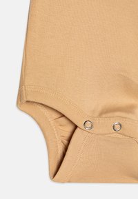Lys beige bomullsbody med en jevn tekstur, med trykknapper nederst og sydd kanter. Enkelt design, uten mønstre.