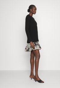 Μαύρο πλεκτό πουλόβερ με ραβδώσεις, μίνι φούστα με floral σχέδιο και ρεβέρ τελείωμα, και μαύρες ανοιχτές μπαλαρίνες. Λείο υλικό, εφαρμοστή γραμμή.