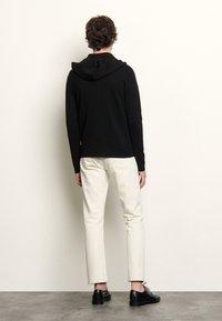 Svart huvad tröja med en figurnära design, kombinerat med gräddfärgade byxor. Utstyrslen fulländas med svarta oxfordskor.