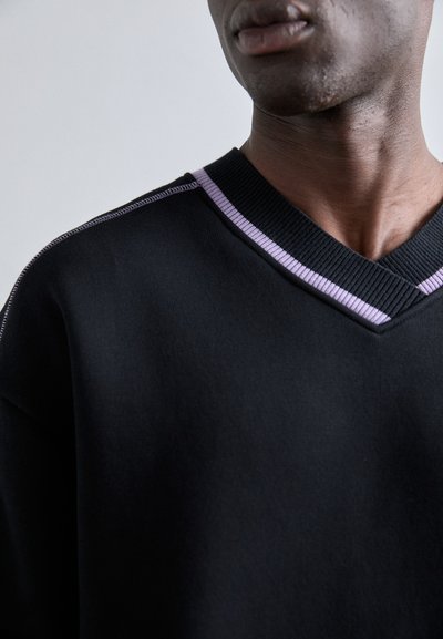 Maglione nero a V con colletto rigato caratterizzato da un accento viola chiaro. Texture liscia e visibile, con una vestibilità comoda e un sottile dettaglio di cucitura.