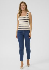 Débardeur à rayures en crème et bleu marine, design ajusté, avec des bretelles larges ; associé à un jean slim bleu et des ballerines claires.