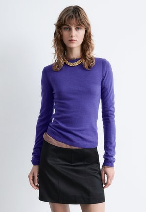 Lila Langarmpullover aus weichem Material mit Rundhalsausschnitt und gerippten Details, kombiniert mit einem schwarzen Leder-Minirock.