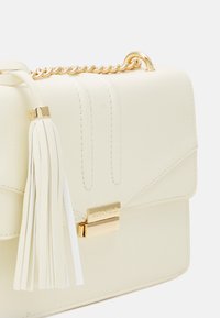 Borsa in pelle color crema con tracolla in catena dorata, chiusura dorata incisa "ANNA FIELD" e un elegante dettaglio a frangia in pelle coordinata.