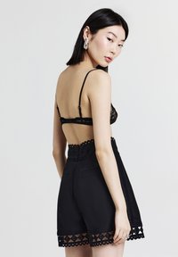 Schwarzer Spitzen-Bralette mit verstellbaren Trägern, kombiniert mit hoch geschnittenen schwarzen Shorts mit gewelltem Saum und Seitentaschen.