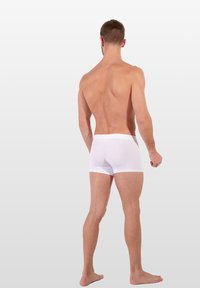 Bílé bavlněné boxerky s těsným střihem, elastickým pasem a hladkým povrchem, z pohledu zezadu na světle šedém pozadí.