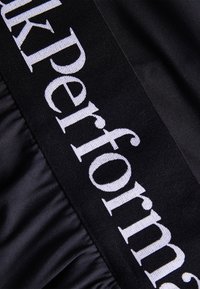 Tela negra con una sección fruncida que presenta el texto bordado en blanco "ukPerform". Textura suave con un diseño elegante.